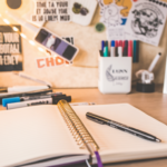 A journal, pen, and vision board arranged on a desk for New Year goal setting and manifestation.