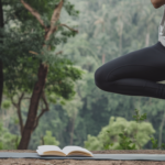 A person practicing yoga outdoors with a fitness journal beside them.